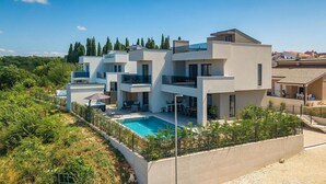Una casa moderna de varios pisos con piscina, rodeada de follaje y un cielo despejado.