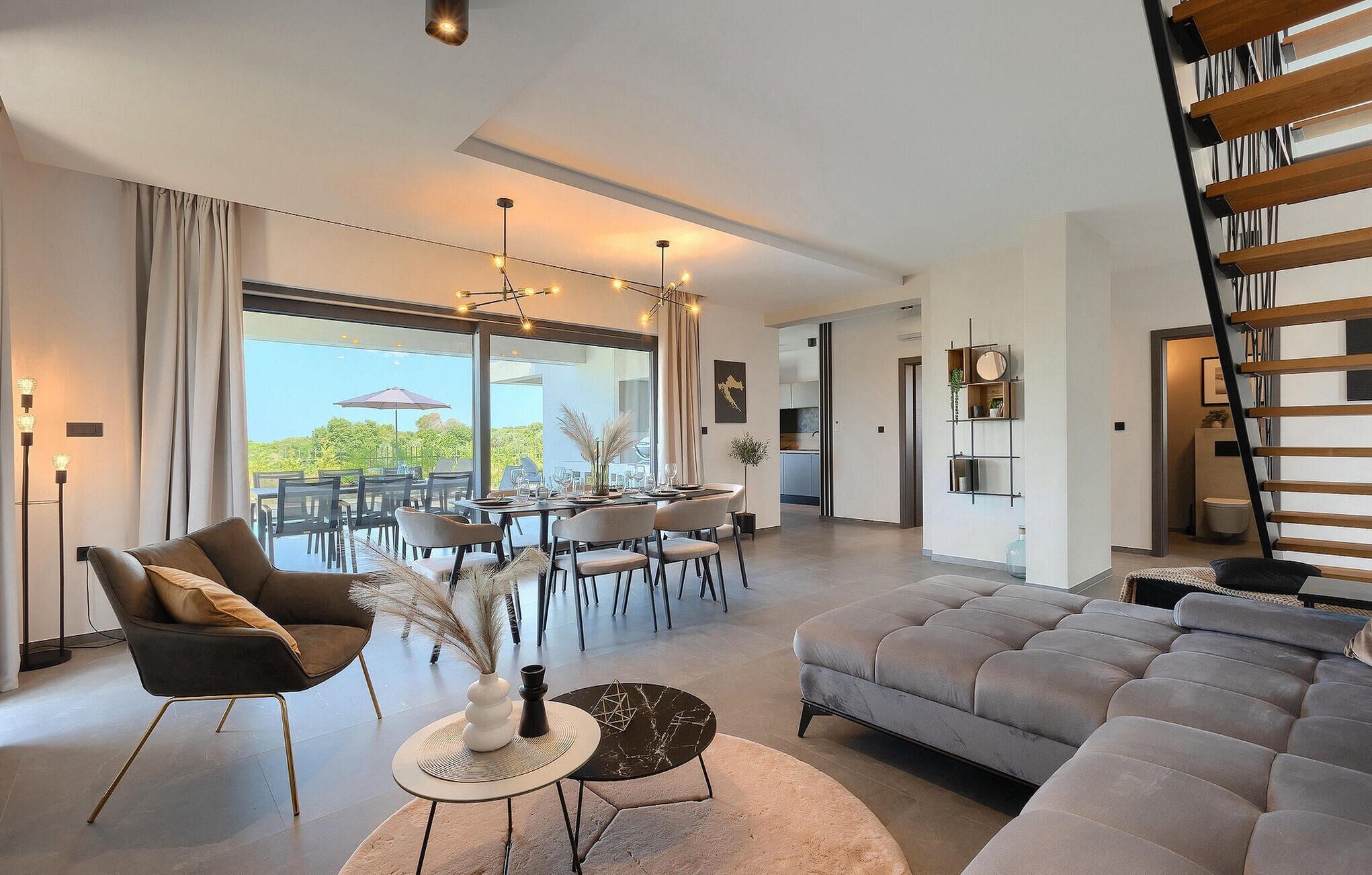 Un salon moderne avec un canapé gris, un coin repas comprenant une table et des chaises, et un escalier.
