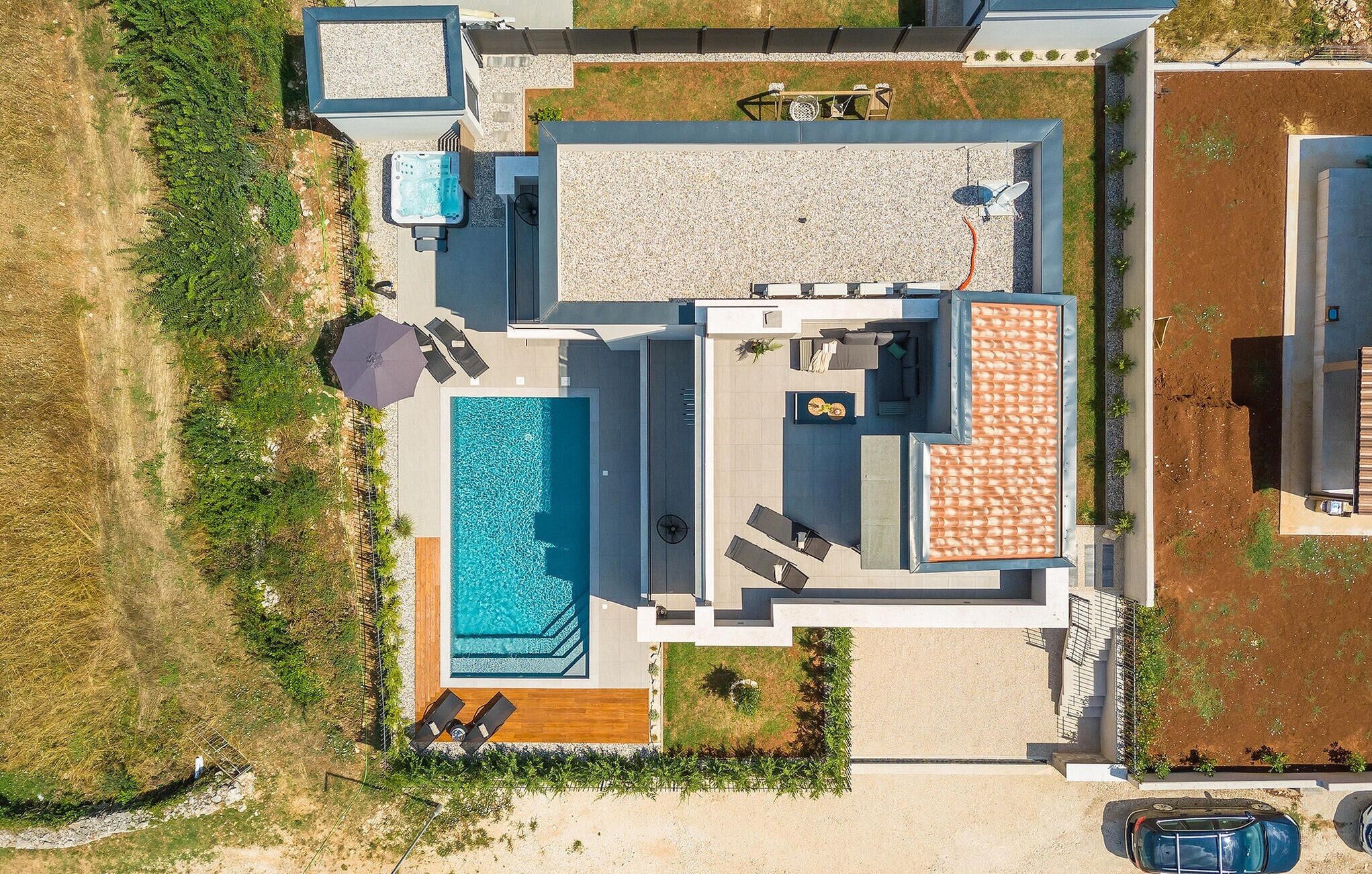 Vue aérienne d’une maison moderne dotée d’une grande piscine rectangulaire, d’un patio couvert et d’une cuisine extérieure séparée.