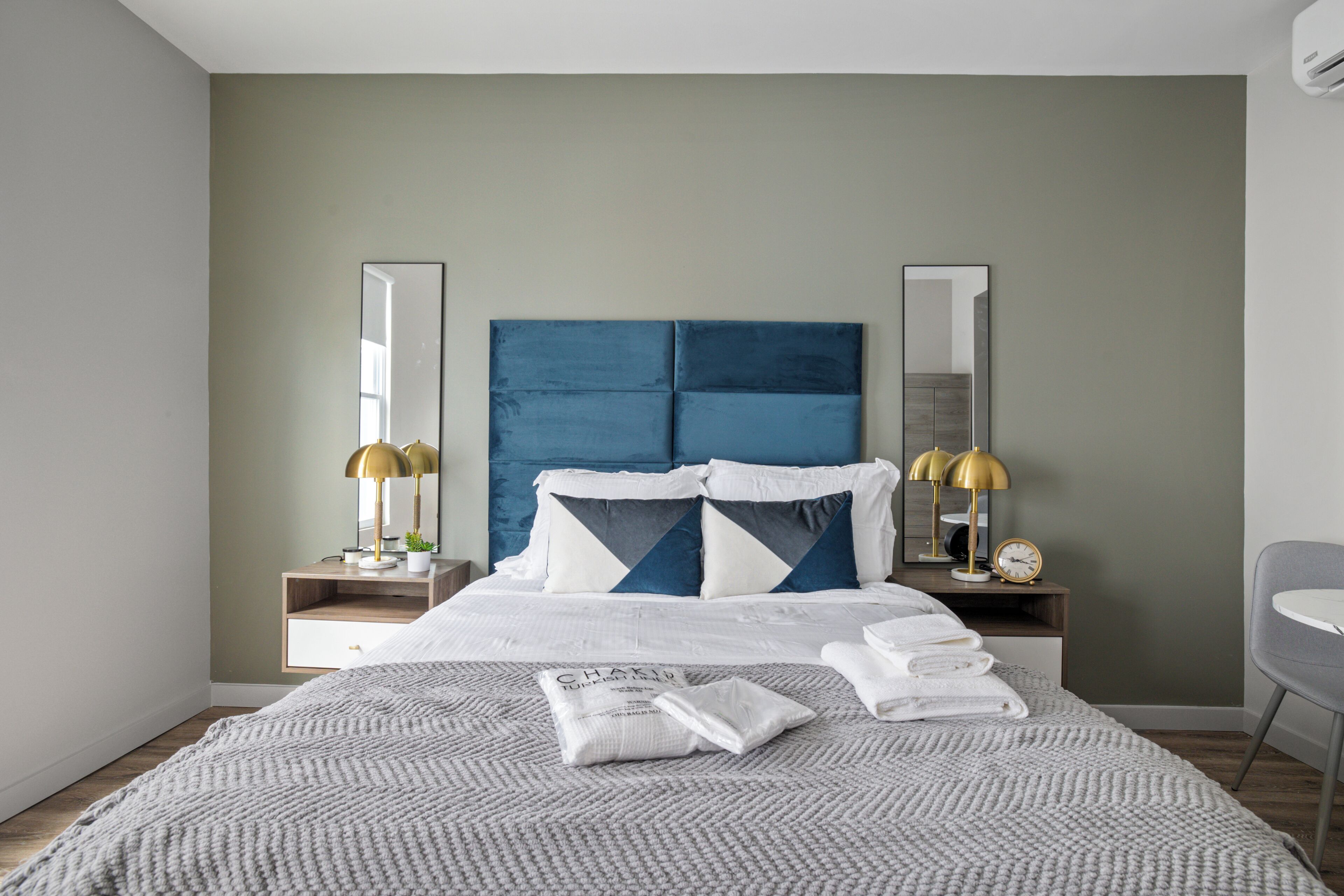 A modern hotel room with a large bed, bedside tables with lamps, a mirror, and a chair.