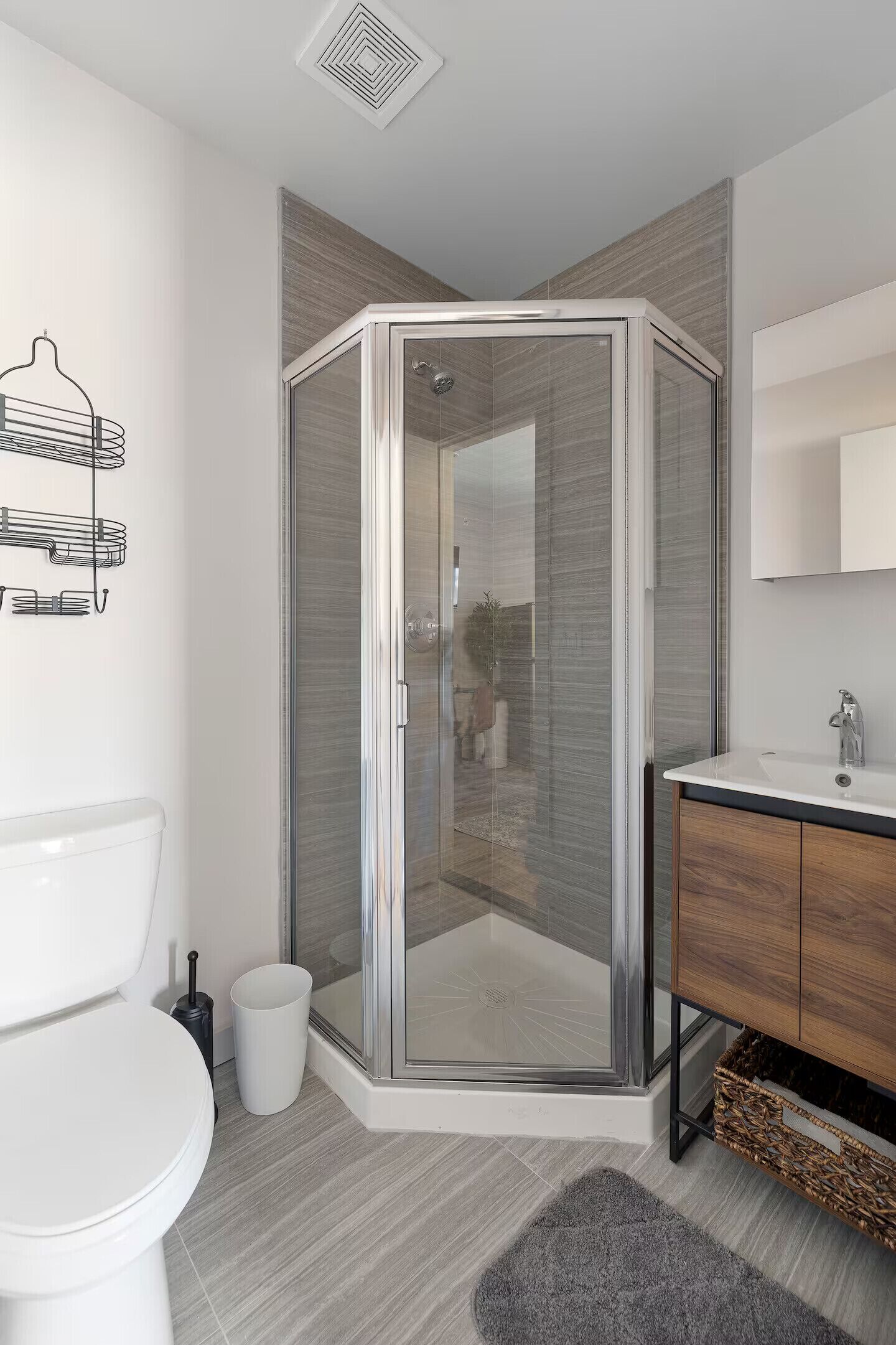 Un bagno moderno con box doccia in vetro, un water bianco, un mobile bagno in legno e un tappeto grigio.