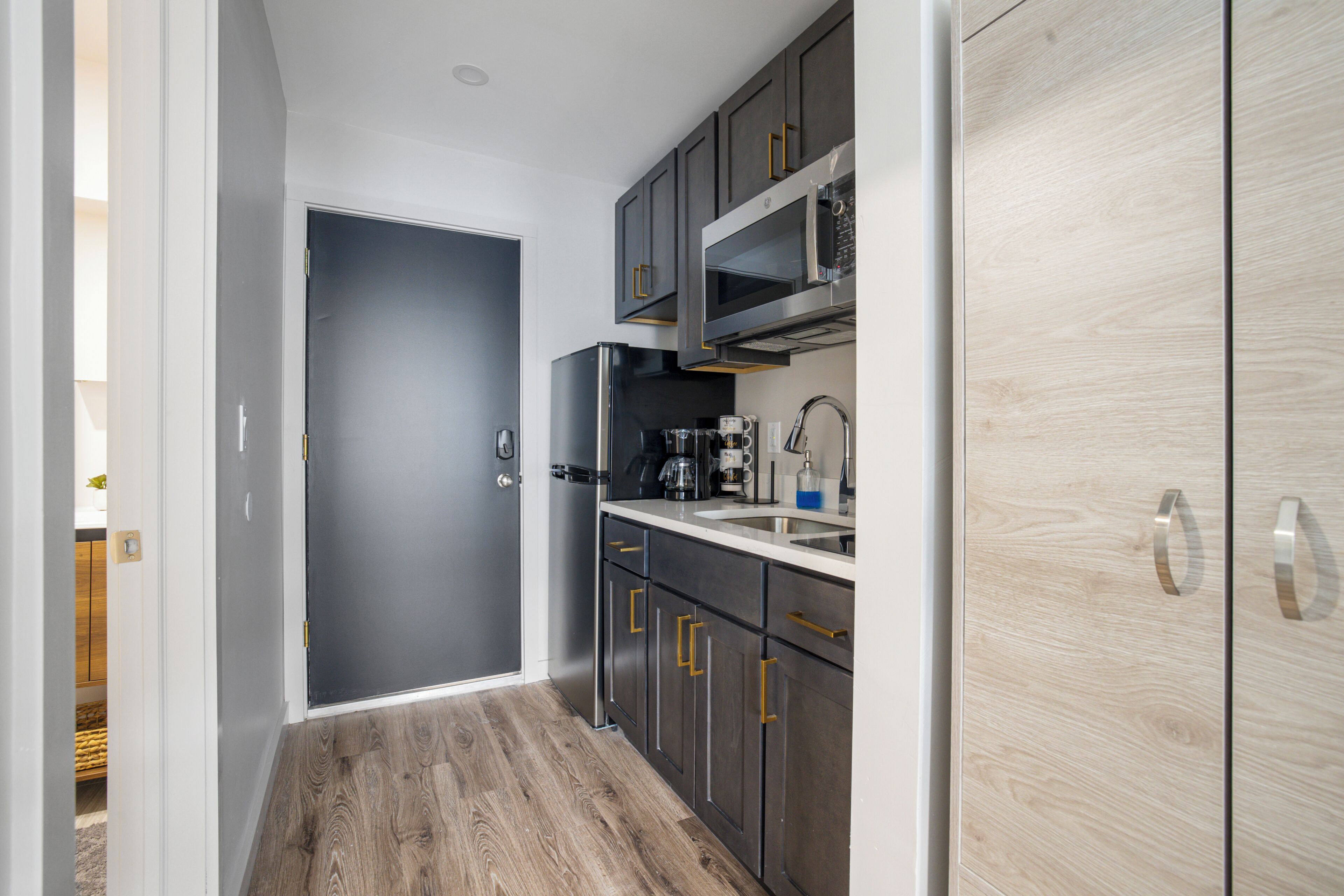 A modern kitchen with grey cabinets, stainless steel appliances, and a wooden floor.