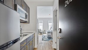 A modern kitchen with stainless steel appliances, a dining area with a geometric rug, and a dark door with a number. - Cottage Suites (Middletown)