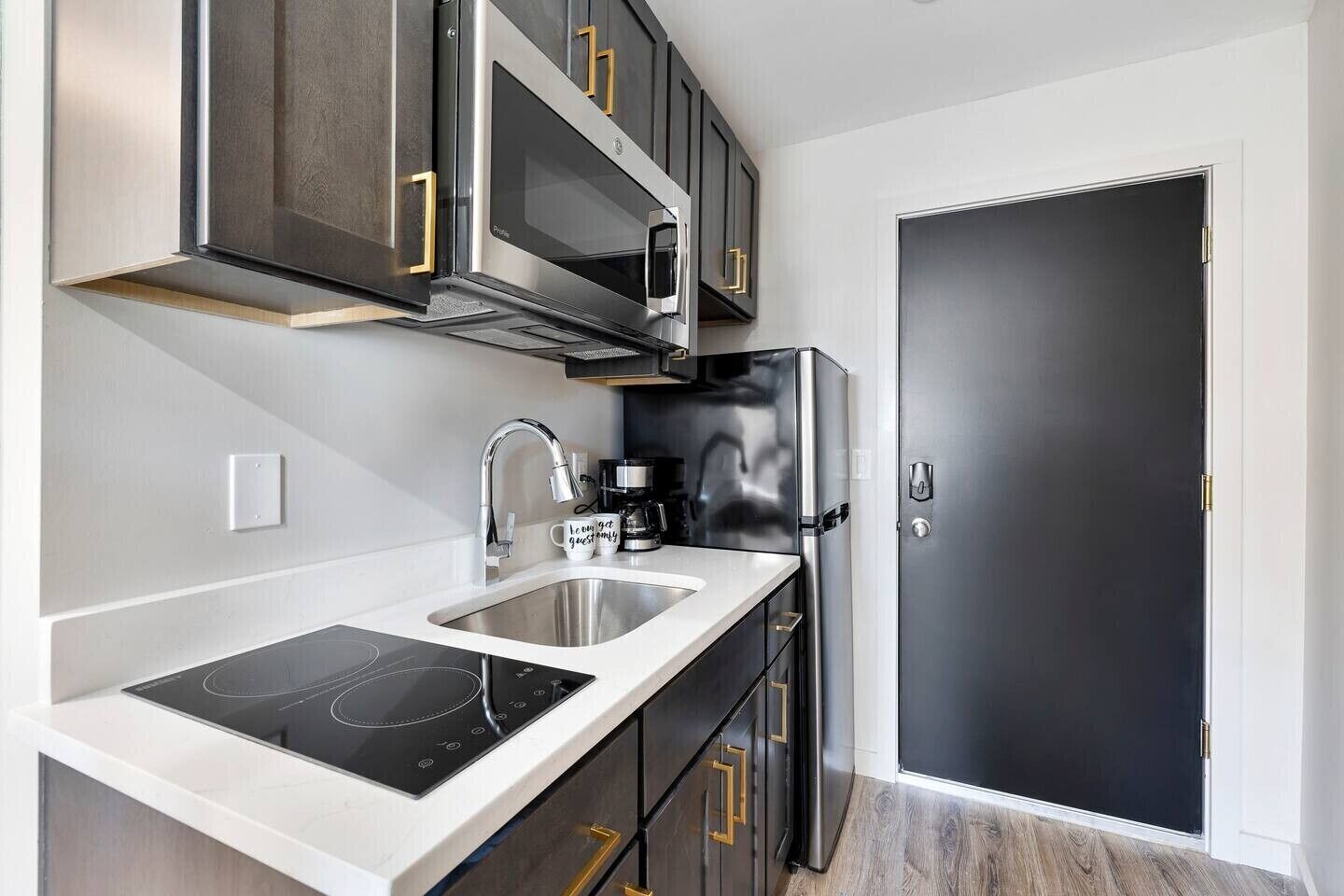 A modern kitchen with a built-in stovetop, stainless steel appliances, and dark cabinetry with gold handles.