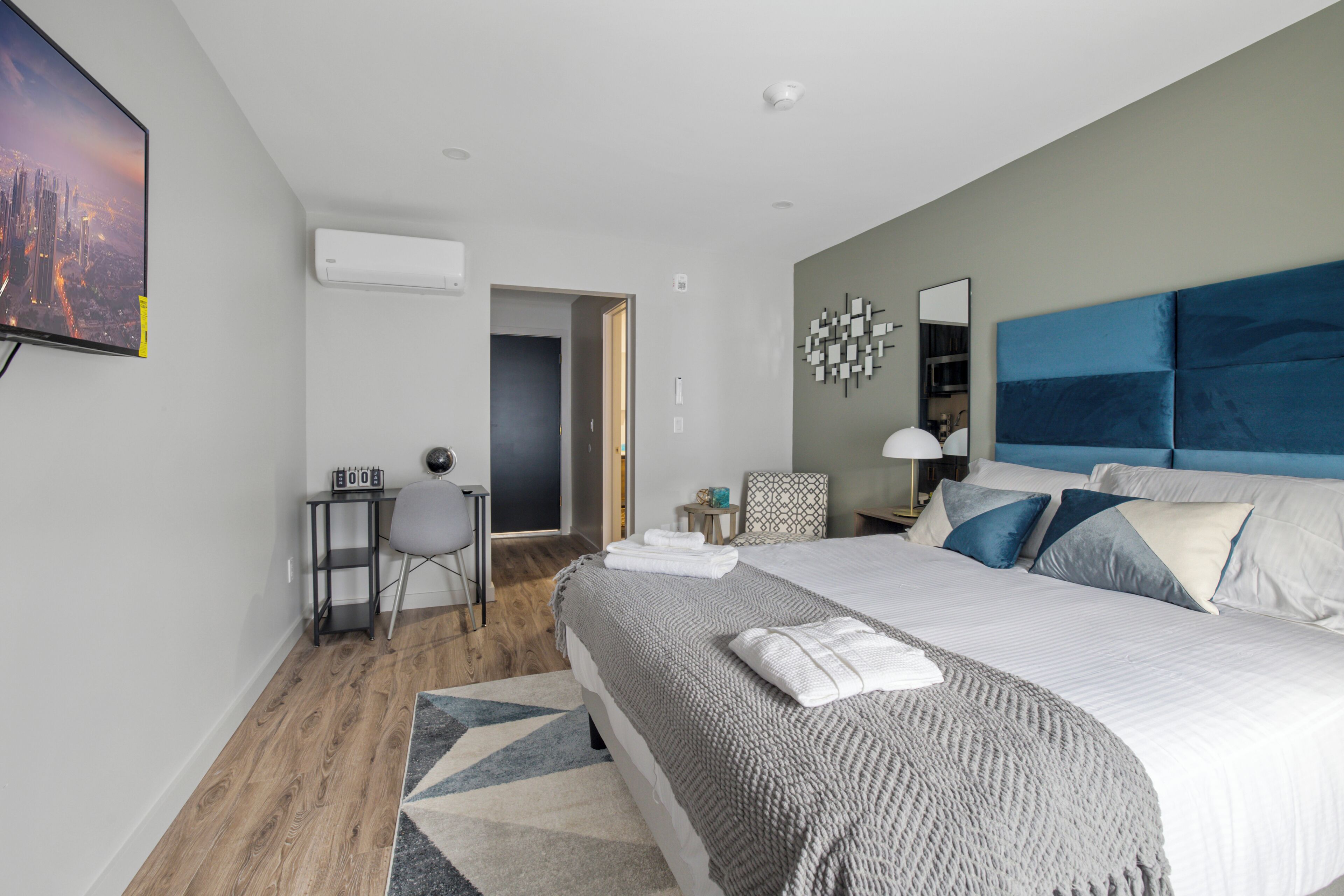 Una camera d'hotel moderna con un letto grande, una scrivania, una sedia e un televisore montato a parete.