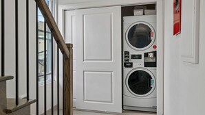 A laundry room with a front-loading washer and dryer, a wooden staircase, and a white door. - Cottage Suites (Middletown)
