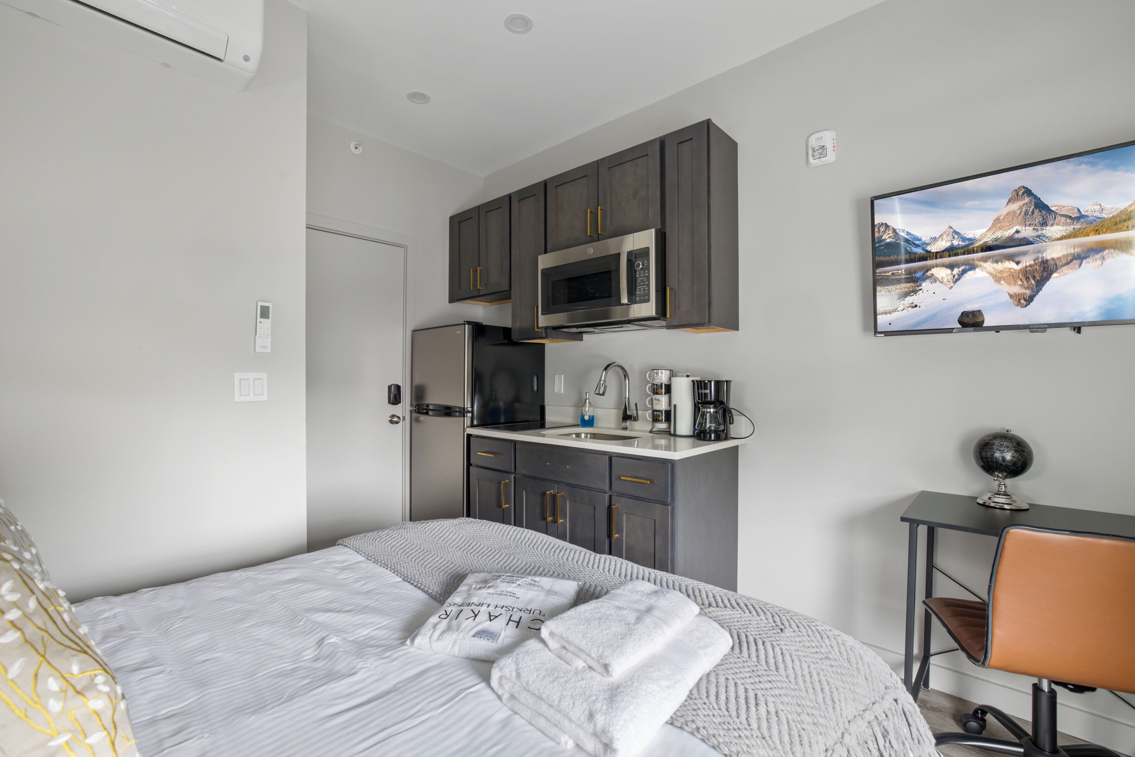 Une chambre d’hôtel moderne équipée d’un lit, d’une kitchenette, d’un bureau et d’un téléviseur fixé au mur.