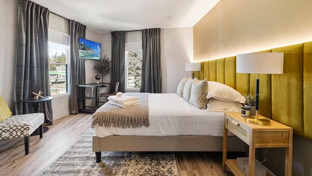 A modern hotel room with a large bed, a desk, a chair, a TV, and a view of the outside. - Cottage Suites (Middletown)