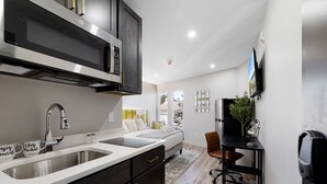 A modern kitchen with a microwave, double sink, and a dining area with a TV and a plant. - Cottage Suites (Middletown)