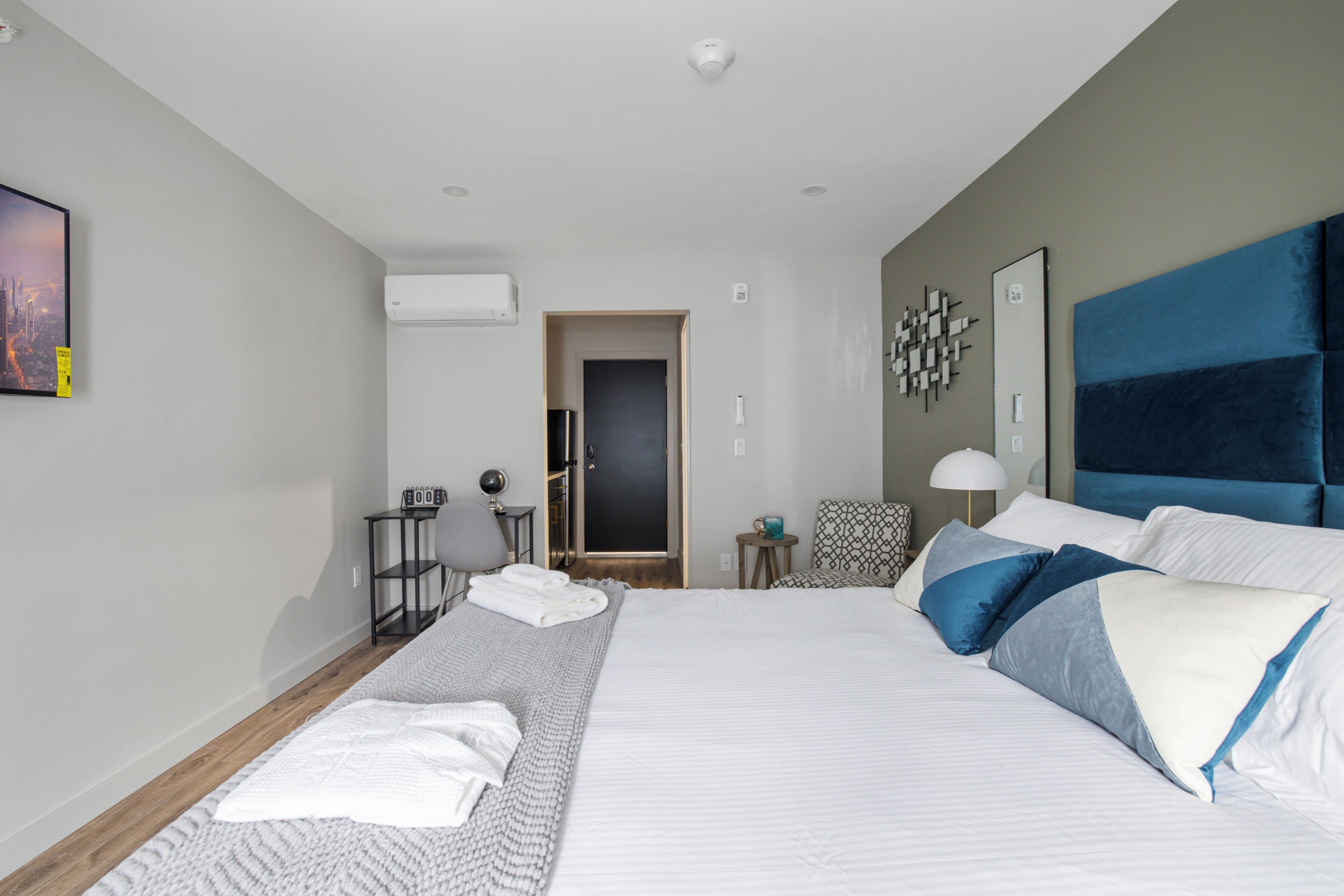 A modern hotel room with a large bed, a bedside table, a chair, and a door leading to a bathroom.