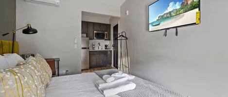 Habitación de hotel con cama, escritorio, silla, lámpara, televisión y kitchenette.