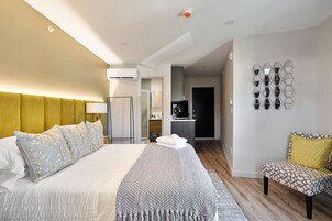 Una habitación de hotel moderna con una cama grande, una mesita de noche, una silla, un baño y una zona de cocina.