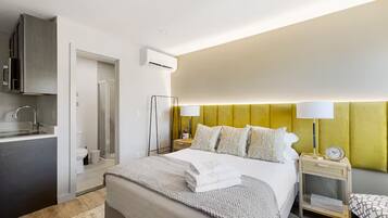 A hotel room with a bed, bedside tables, a nightstand, a lamp, a clock, a mirror, a wardrobe, a sink, and an air conditioning unit.