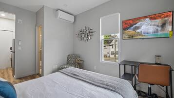 Un dormitorio con cama, escritorio, silla, ventana y televisor instalado en la pared.