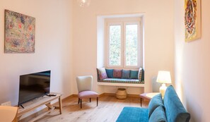 Un salon comprenant un téléviseur, un canapé, un fauteuil, un banc de fenêtre et une lampe.