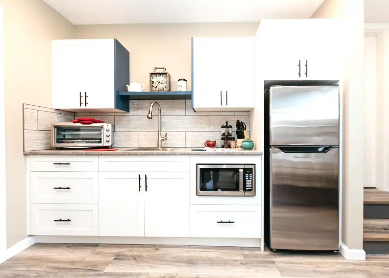 A modern kitchen with white cabinets, a stainless steel refrigerator, a built-in microwave, and a toaster oven.
