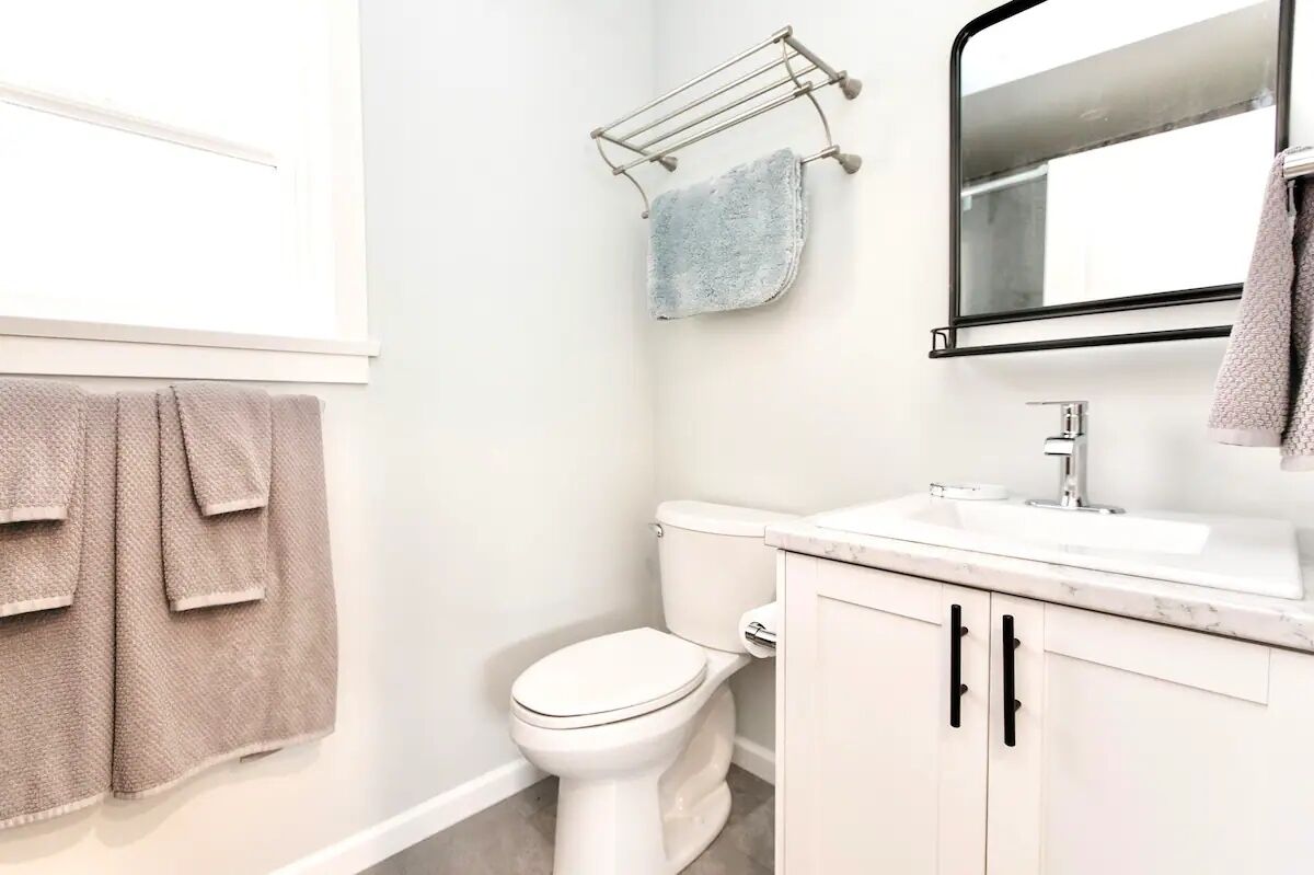 A bathroom with a toilet, sink, and mirror. There are towels hanging on a rack and a towel on the wall.