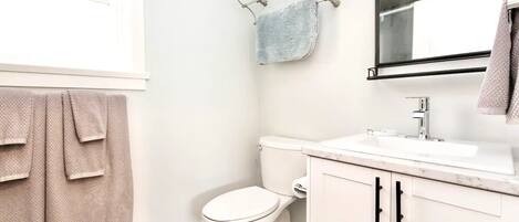 A bathroom with a toilet, sink, and mirror. There are towels hanging on a rack and a towel on the wall.