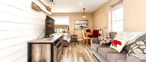 A compact living space with a kitchenette, a sofa with decorative pillows, a dining area, and a painting on the wall.