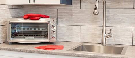 A kitchen with a built-in toaster oven, a stainless steel sink, and white cabinets.