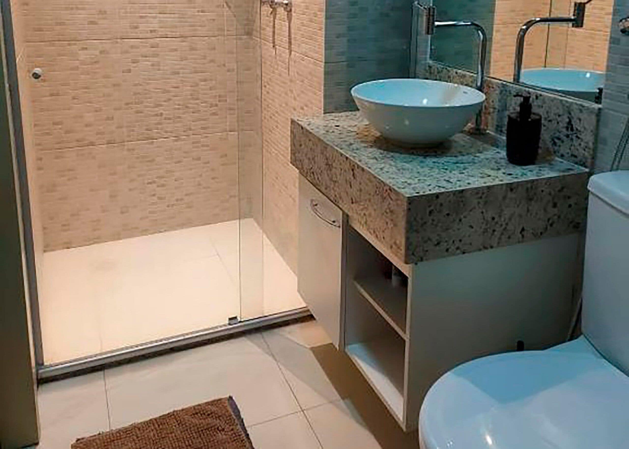 Casa de banho com cabine de duche em vidro, lavatório branco e sanita.