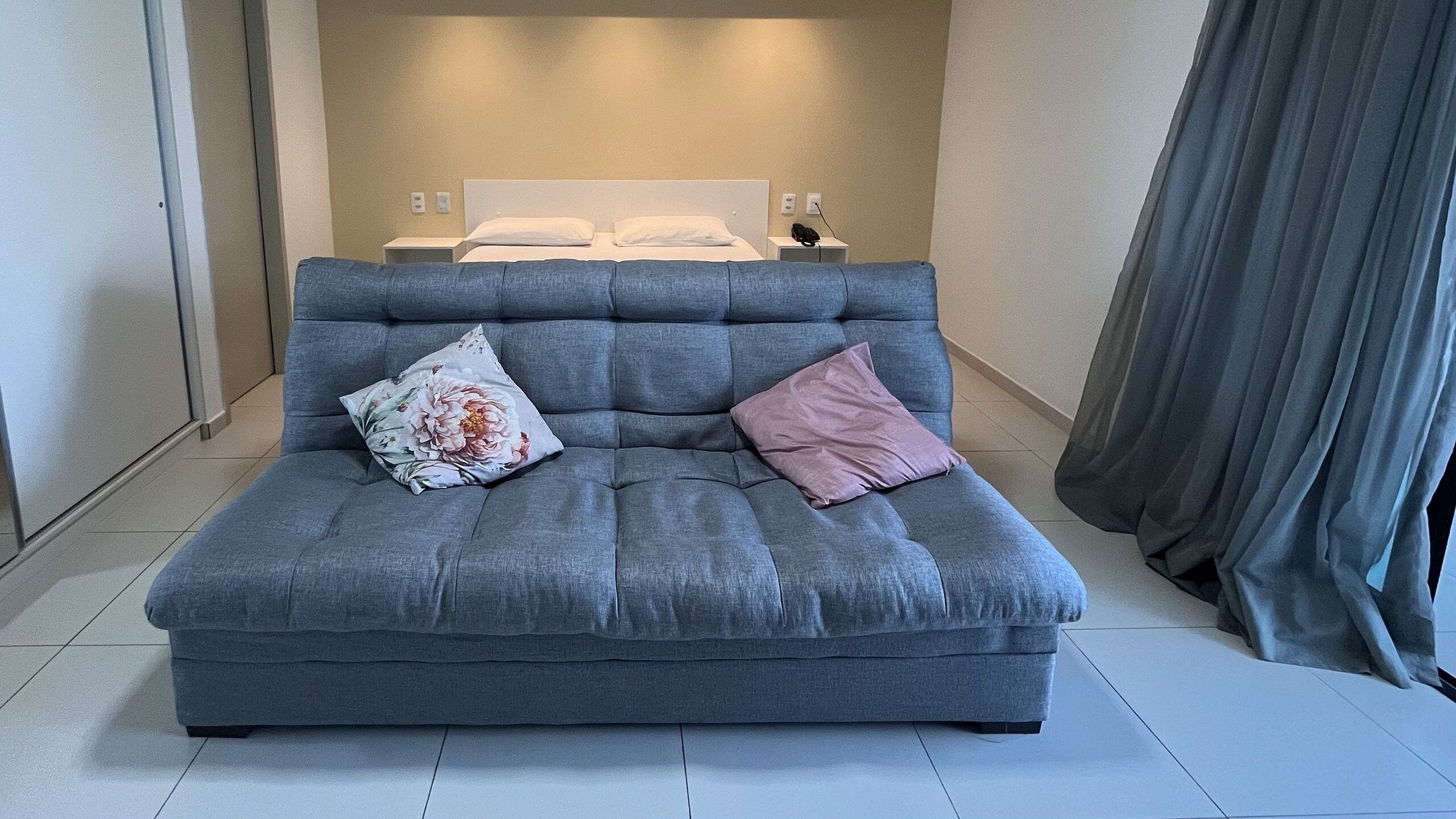Un sofá gris con cojines florales y rosados en una habitación de hotel.