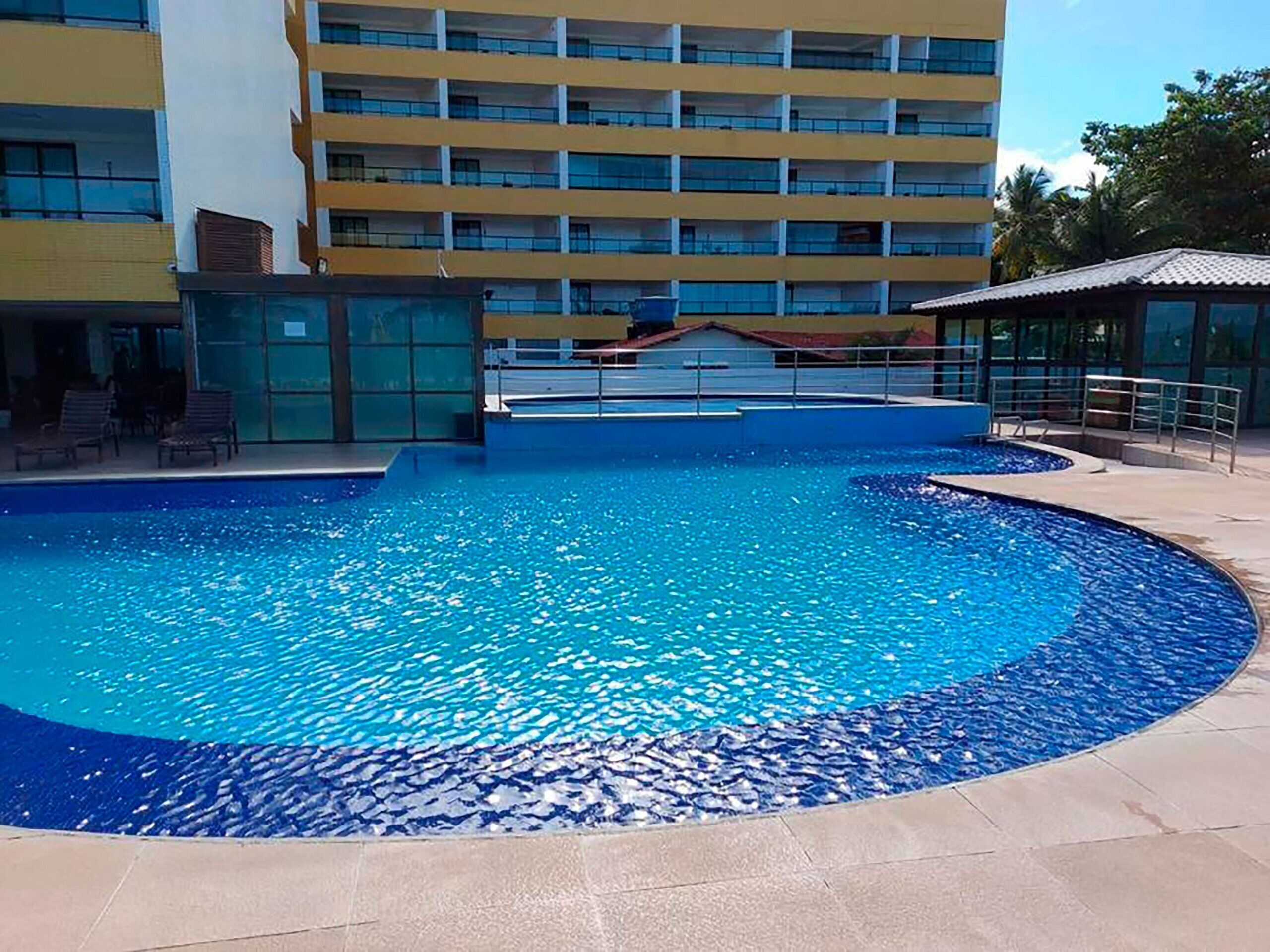 A swimming pool with a tiled deck, surrounded by a building with multiple balconies.