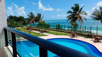 Piscina com vista para o oceano, rodeada por palmeiras e cadeiras de descanso.