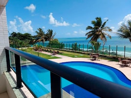 A pool with a view of the ocean, surrounded by palm trees and lounge chairs.