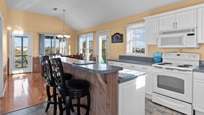A kitchen with a wooden island, white cabinets, a microwave, an oven, and a view of the outdoors through large windows. - 5591- Beach, Please! - Soundside Escape in Nags Head | Dog Friendly (Nags Head)