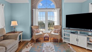 A living room with a large window, two wicker chairs, a sofa, a TV, and a cabinet. - 5591- Beach, Please! - Soundside Escape in Nags Head | Dog Friendly (Nags Head)