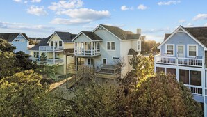 A row of coastal houses with balconies, surrounded by dense shrubbery. - 5591- Beach, Please! - Soundside Escape in Nags Head | Dog Friendly (Nags Head)