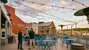 Une terrasse extérieure avec des chaises et des tables bleues, des guirlandes lumineuses suspendues au-dessus, et un bâtiment sur lequel on peut lire l’inscription : « Services de santé universitaires ».