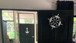 Un ingresso decorato con una ruota di timone, un pavimento piastrellato e vista su una cucina con un piano cottura.