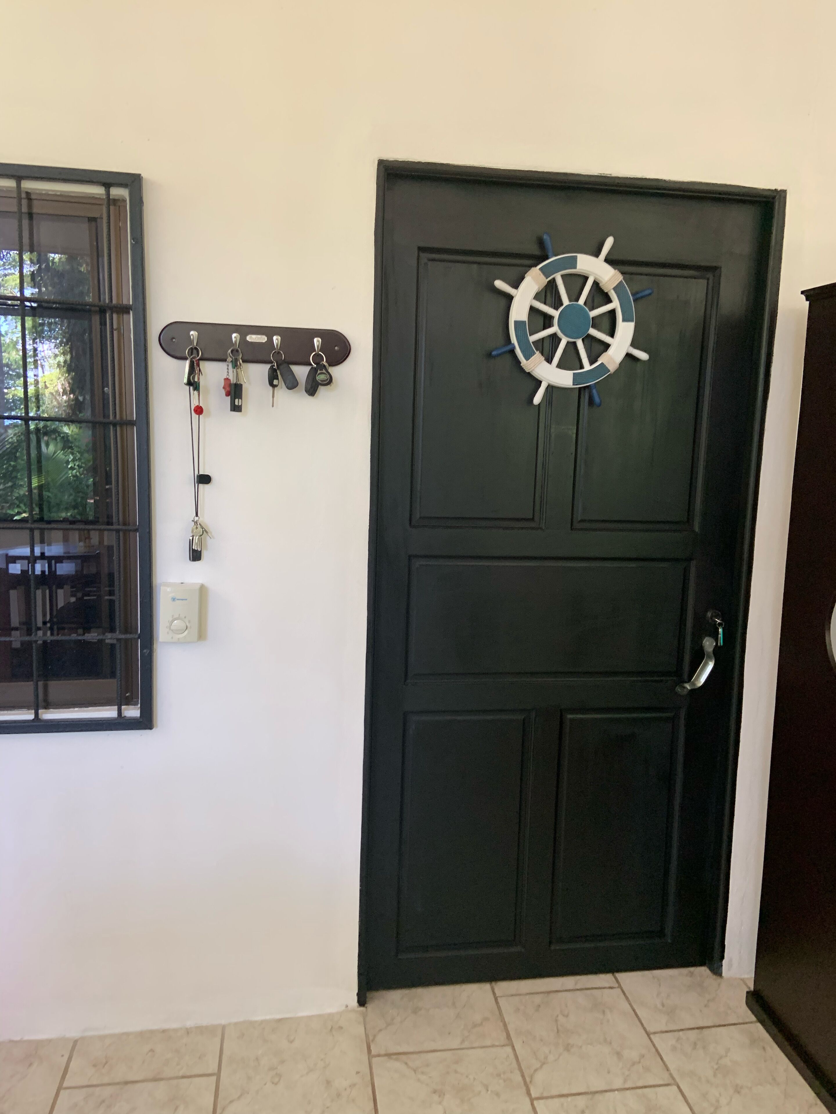 A dark wooden door with a ship's wheel decoration, a key rack with keys, and a window with bars.
