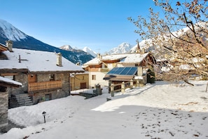 A snow-covered village with traditional stone buildings, a wooden staircase, and a solar panel on a roof.