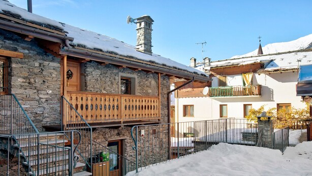 Ein Steinhaus mit einem hölzernen Balkon, einer Treppe und einem schneebedeckten Boden.