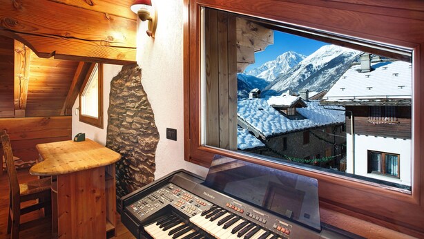 A wooden interior with a piano, a stone wall, and a window with a snowy mountain view.