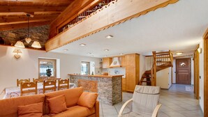 A cozy living area with a sofa, a chair, a wooden staircase, and a kitchen area.