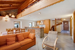 A cozy living area with a sofa, a chair, a wooden staircase, and a kitchen area.