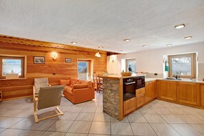 A cozy cabin interior with a wooden interior, a stone island in the kitchen, and a view through the window.
