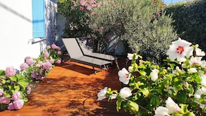 Una terraza de madera con una silla de descanso, rodeada de exuberante vegetación y plantas en flor.