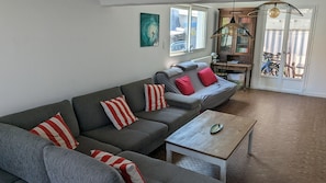 En stue med en grå hjørnesofa, røde og hvide stribede puder, et træsofabord og et stort vindue med udsigt.