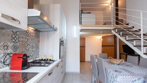 Cocina compacta con estufa a gas, microondas y cafetera roja.  Comedor con mesa y sillas, y escalera que sube a un nivel superior.