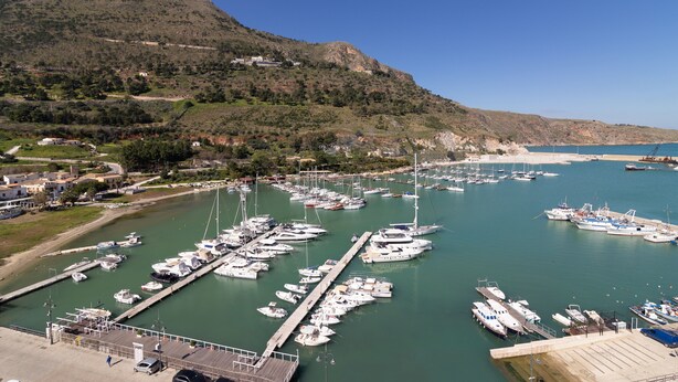 Un puerto deportivo con numerosas embarcaciones amarradas, rodeado de un paisaje montañoso y cielo despejado.