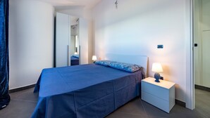 Een slaapkamer met een bed, een nachtkastje met een lamp, een spiegel en een deur.