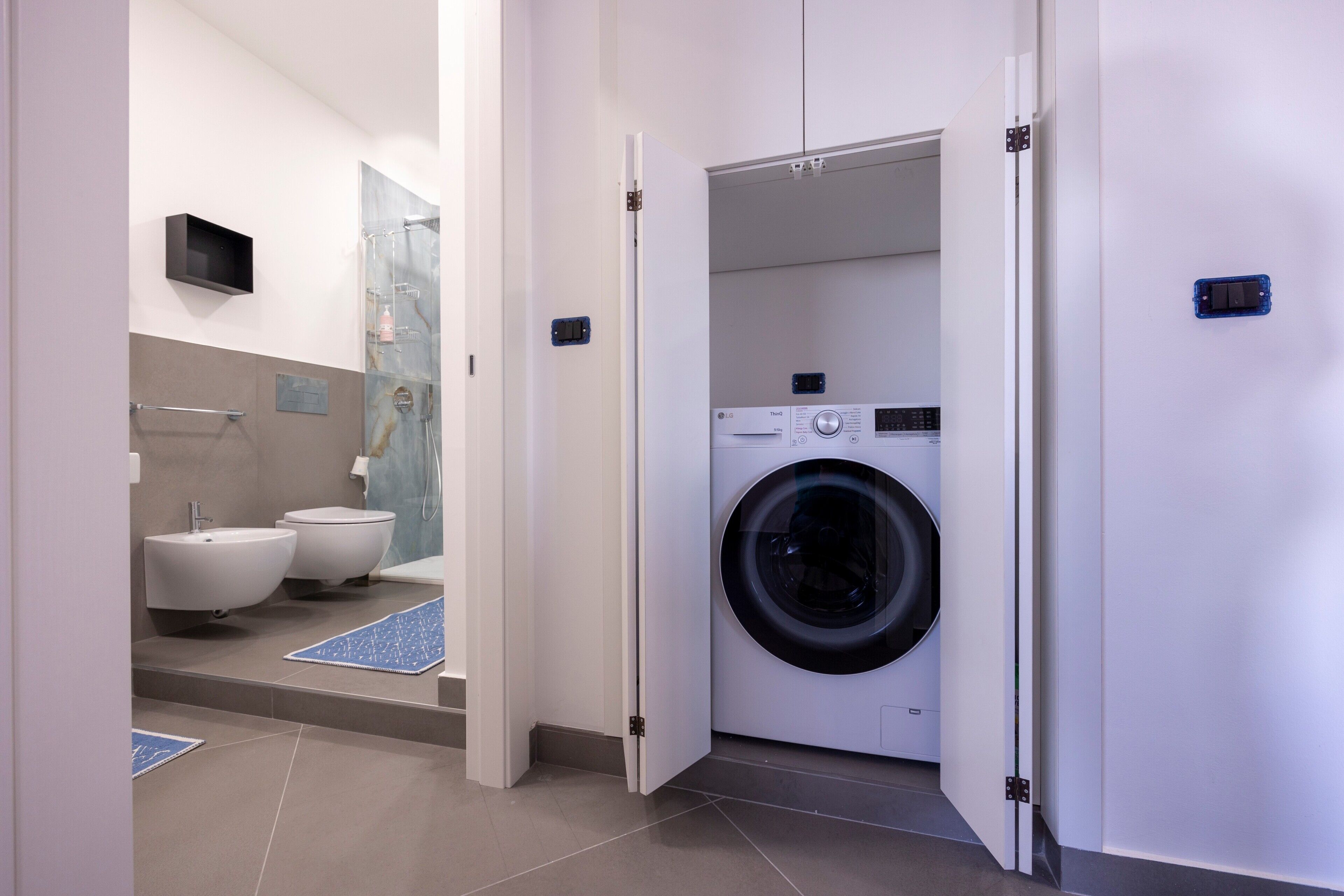 A modern bathroom with a washing machine, bidets, and a shower.