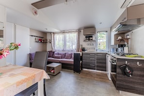 Un espacio habitable compacto con sofá, mesa de comedor, kitchenette y ventana con cortinas.