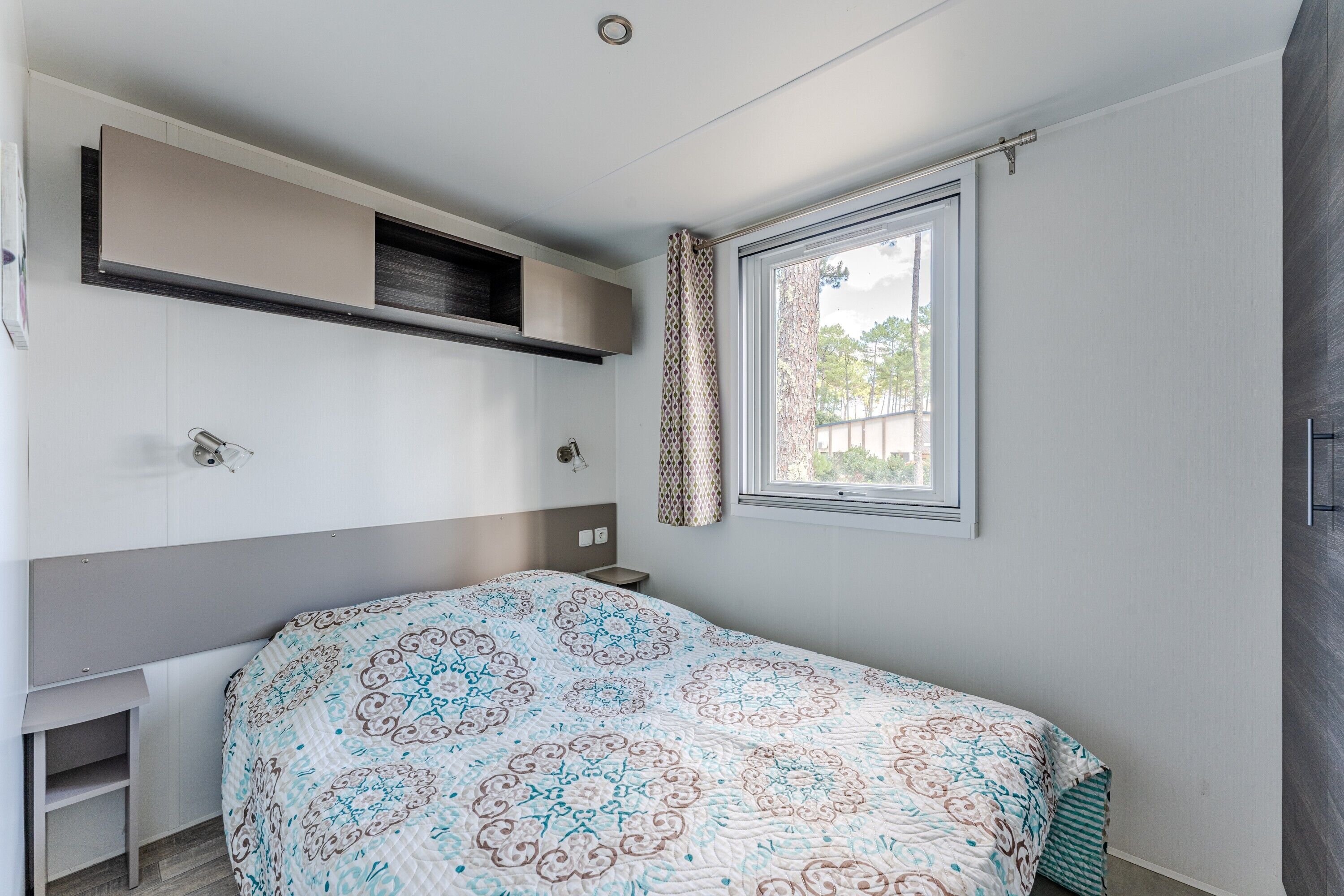 A bedroom with a bed, a window, a built-in shelf, and a bedside table.