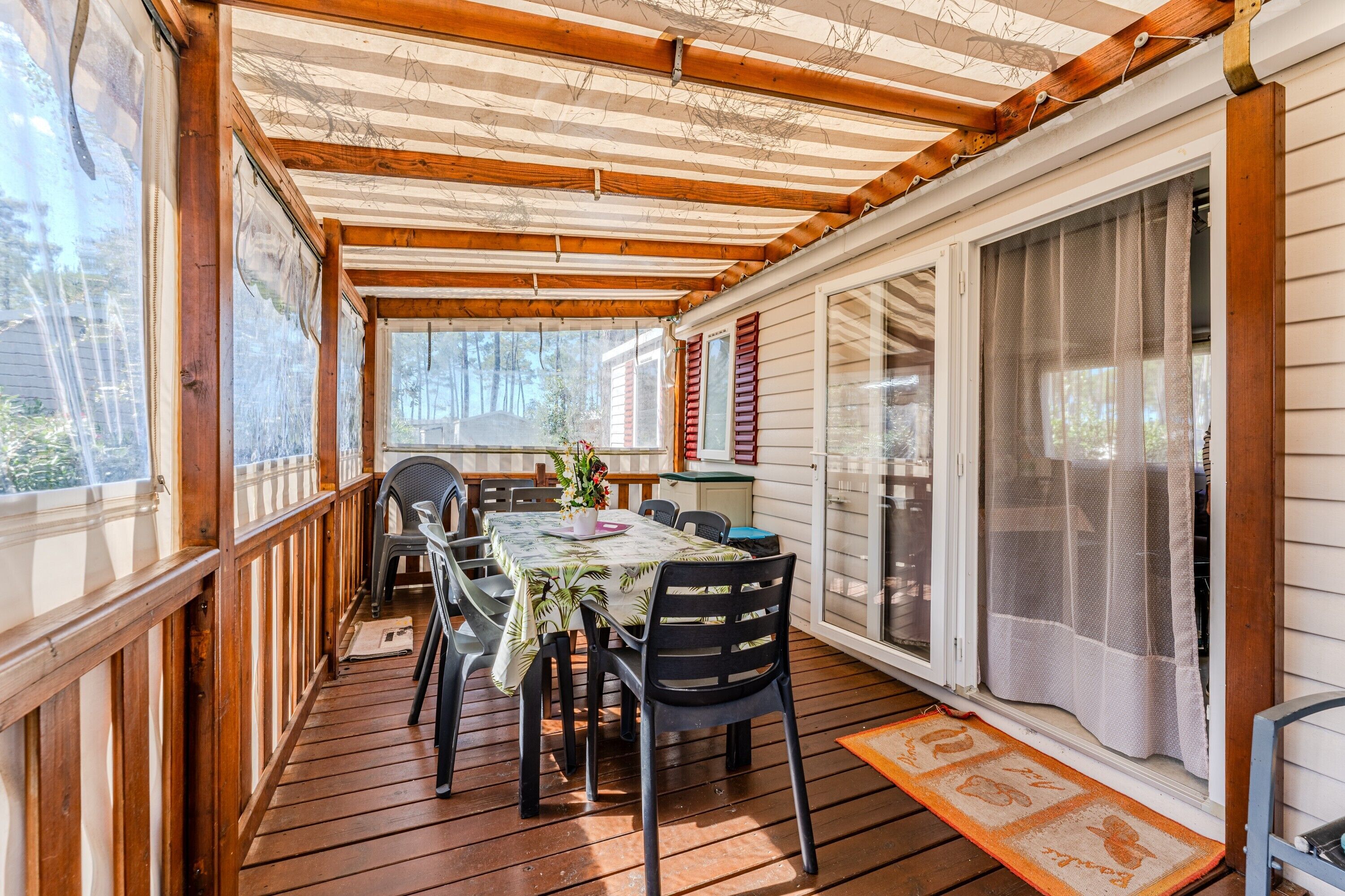 Une véranda avec une table et des chaises, une fenêtre avec des volets et une porte avec un rideau.